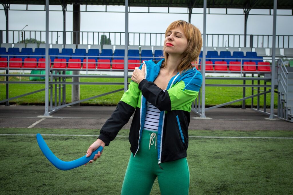 A woman holds a blue and green bat, symbolizing strength in shoulder recovery exercises for bursitis.
